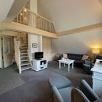 Living room with sofa, armchairs, and staircase to gallery. Dining table and TV are present.