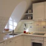 Kitchen with white cabinets, sink, stove, and oven under sloped ceiling.