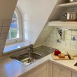 Kitchen with stainless steel sink, worktop and window. On the worktop is a wooden board with vegetables.