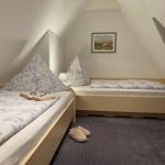 Two beds with blue-and-white bedding, wall picture, and slippers on carpet.