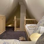 Bedroom with sloped ceiling, bed, wardrobe, and staircase.