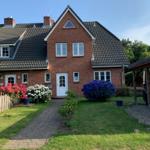 Rotes Backsteinhaus mit weißen Fenstern und blühenden Blumen im Vorgarten.