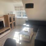 Wohnzimmer mit Sofa, TV und Tisch. Fenster mit Rollladen und Deckenleuchte.