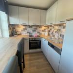 Küche mit weißen Schränken, Holzoberfläche und Mosaikwand. Einbauherd, Spüle und Kaffeemaschine.