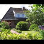 Haus mit Ziegeldach, umgeben von grünem Garten und blühenden Sträuchern.