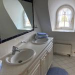 Badezimmer mit zwei Waschbecken, Spiegel und Fenster mit weißen Vorhängen.