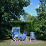 Außenbereich mit blau-weißen Strandkörben und Tisch auf Steinplatten umgeben von Bäumen.