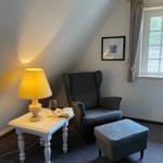 Ein Raum mit Sessel, Beistelltisch, Lampe und Fenster. Auf dem Tisch steht ein Glas Wein.