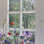 Ein Fenster mit Blumenstrauß im Vordergrund und Blick auf einen blühenden Garten.