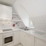 Küche mit weißen Schränken, Edelstahlspüle und Kochfeld. Dachschrägen Decke und Fenster.