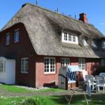 Rotes Backsteinhaus mit Strohdach, weißer Eingang und Gartenmöbel.