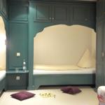 Zimmer mit zwei Betten in grünen Holzrahmen und einem Sitzbereich mit floraler Polsterung.