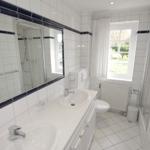 Badezimmer mit Dusche, Waschbecken und Toilette. Weiße Fliesen und Spiegel.