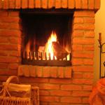 A fireplace with burning wood, surrounded by red bricks and a basket with firewood.