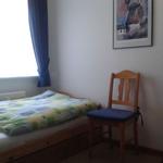 A room with a bed, a chair, and a window with a curtain.