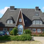 A two-story house with red brick walls and a dark gabled roof. Blue door and windows are visible.