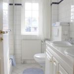 Badezimmer mit Dusche, Toilette, Waschbecken und Fenster mit Vorhang.