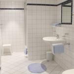 Badezimmer mit Dusche, Waschbecken und Toilette. Weiße Fliesen und blau-weiße Handtücher.