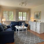 Wohnzimmer mit zwei blauen Sofas, weißem Tisch und Fenstern mit Vorhängen.