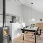 Dining area with table, chairs, and wood stove. Background: kitchen and glass doors.