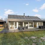 Modern villa with large wooden deck, seating, and view of the garden.