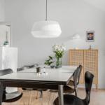 Dining room with table, chairs, and lighting. Background: cabinet and window.