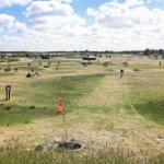 Golf course with bunkers and picnic tables under blue sky.