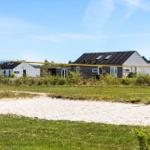 Volleyball net in front of beach house with green grass and sand.