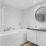 Bath with whirlpool, sink, and round mirror. Window with plant.