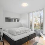 Bedroom with double bed, chair, and balcony door. Trees are visible outside.