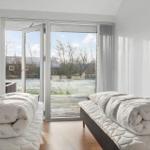 Two beds with duvets in a room with view of a terrace and landscape.