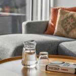 A water pitcher and a book are on the table. In the background, there is a sofa with cushions.