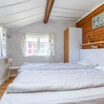 Schlafzimmer mit Bett, Fenstern, Kleiderständer und Holzwand.