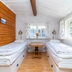 Zwei Einzelbetten mit Schubladen, Holzwand, Fenster und Tisch im Raum.