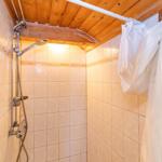 Dusche mit Duschbrause und weißen Vorhängen an Holzdecke.