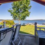 Terrasse mit Gartenmöbeln und Blick auf See und Holzsteg.