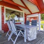 Terrasse mit Tisch, Stühlen und Grill. Roter Holzaufbau und Sicht in die Küche.