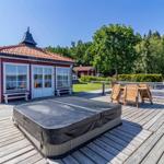 Rotes Haus mit Terrasse, Whirlpool und Holzmöbeln am Wasser.