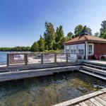 Rotes Holzhaus am Wasser mit Terrasse und Liegeflächen.