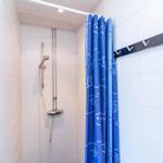 Dusche mit blauem Vorhang und silberner Duschkopf an weißen Fliesen.