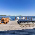 Holzterrasse mit Liegestühlen, Tisch und Whirlpool am Wasser.