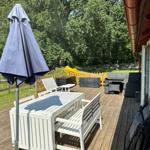 Terrasse mit weißem Tisch, Stühlen und geschlossenem Sonnenschirm. Im Hintergrund Grünfläche und Spielplatz.