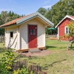 Ein kleines Haus mit roter Tür und Terrakottadach steht auf einer Wiese neben einem größeren roten Haus.