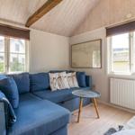 Ein Wohnzimmer mit blauem Sofa, Holzboden und zwei Fenstern mit Blick auf Häuser.