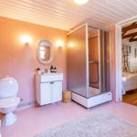 Badezimmer mit Dusche, Waschbecken und Toilette. Blick in das Schlafzimmer mit zwei Betten.