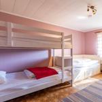Zimmer mit Doppelstockbett und Einzelbett, rosa Wände und Holzboden.