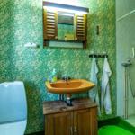 Badezimmer mit grünem Tapetenmuster, Waschbecken auf Holzschrank, Dusche und Toilette.