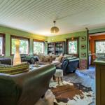 Wohnzimmer mit braunen Ledersofas, Holzboden und großen Fenstern mit Blick auf Bäume.