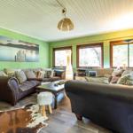 Wohnzimmer mit zwei Ledersofas, Holzboden und grünen Wänden. Fenster und Wandbild sichtbar.