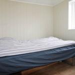 Ein Schlafzimmer mit Bett, Fenster und vertikal verkleideten Wänden.